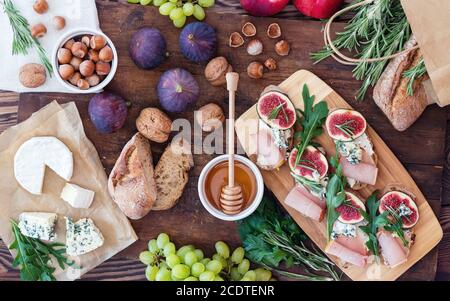 Sandwiches mit Ricotta, frischen Feigen, Prosciutto, Rosmarin und Blauschimmelkäse, Walnüssen und Honig auf rustikalem Holzbrett über schwarzem B Stockfoto