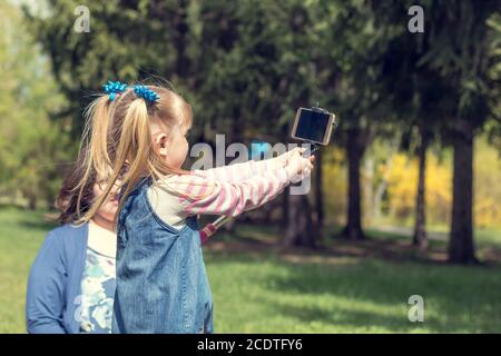 Süße kleine blonde Mädchen mit zwei pferdeschwänze unter selfie im Stadtpark auf einer Feder sonnigen Tag Stockfoto