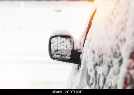 Das Auto ist mit Schnee bedeckt. Schnee auf Rückspiegel. Konzept des Fahrens im Winter mit Schnee auf der Straße. Getöntes Foto mit Stockfoto