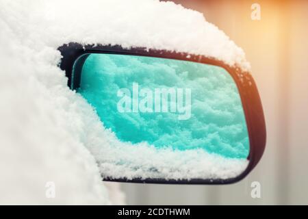 Das Auto ist mit Schnee bedeckt. Schnee auf Rückspiegel. Konzept des Fahrens im Winter mit Schnee auf der Straße. Getöntes Foto mit Stockfoto