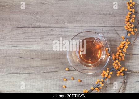 Herbst gesundes Heißgetränk Konzept. Zweig des gemeinen Sanddorns mit der Beere, Tasse Tee, auf hellem hölzernen Hintergrund. Getöntes Foto Stockfoto