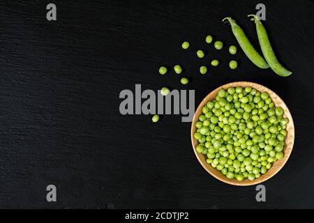 Körner frische grüne Erbsen in Houten auf einen schwarzen Stein Oberfläche. Ansicht von oben, kopieren. Gesunde Ernährung Konzept. Stockfoto