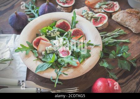 Leicht diätetische Salate mit Rucola, Feigen und Blauschimmelkäse auf einer braunen Holzoberfläche. Sandwiches mit Ricotta, frischen Feigen, Prosciutto, r Stockfoto