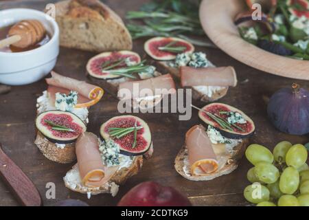 Leicht diätetische Salate mit Rucola, Feigen und Blauschimmelkäse auf einer braunen Holzoberfläche. Sandwiches mit Ricotta, frischen Feigen, Prosciutto, r Stockfoto