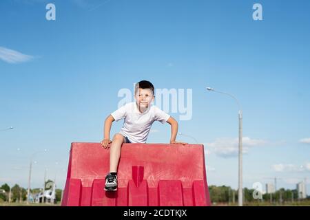 Junge sitzt auf Straßenzaun, Konzept des Spielens auf verbotenes Gebiet Stockfoto