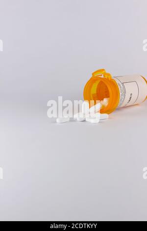 Pille Flasche liegt auf seiner Seite mit weißen Tablette Pillen Auf weißem Hintergrund mit Platz für die Kopie in auslaufen Hochformat Stockfoto