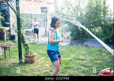 Kinder spielen im Garten mit Gewehren und Wassergewehren An einem sonnigen Sommertag Stockfoto