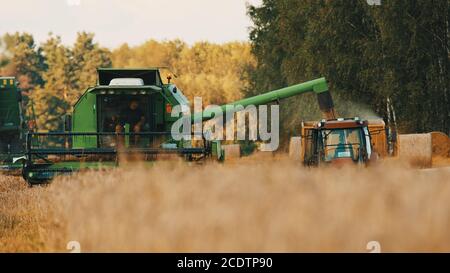 Warschau, Polen 10.08.2020 Moderne Mähdrescher thrasher und Traktor mit Trail arbeiten auf dem Weizenfeld. Nahaufnahme. Hochwertige 4k-Aufnahmen Stockfoto