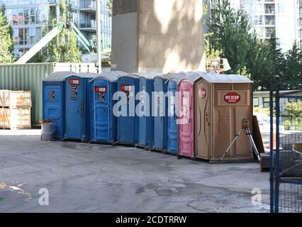 Tragbare Toiletten, blau, rosa und braun, sind für den Einsatz auf einer Baustelle in Vancouver, British Columbia, Kanada aufgereiht. Die rosa Toiletten sind Stockfoto