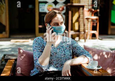 Junges Mädchen mit Maske im Gespräch am Telefon in der Öffentlichkeit Stockfoto