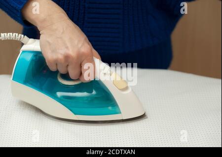Frau bügelt weiße Kleidung auf dem Bügelbrett. Nahaufnahme. Horizontale Aufnahme. Stockfoto