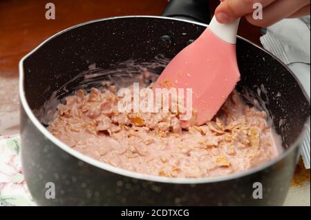 Von Hand gemachter Cornflakes in geschmolzener Erdbeerschokolade in der Pfanne. Nahaufnahme. Horizontale Aufnahme. Stockfoto