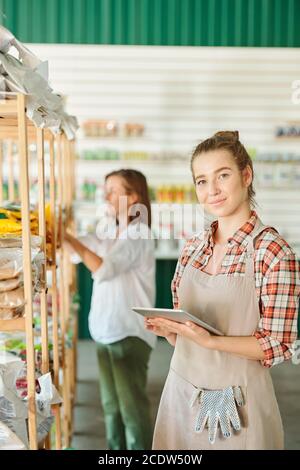 Junge hübsche weibliche Assistentin der Gartenarbeit Supermarkt in Arbeitskleidung mit Tablet Stockfoto