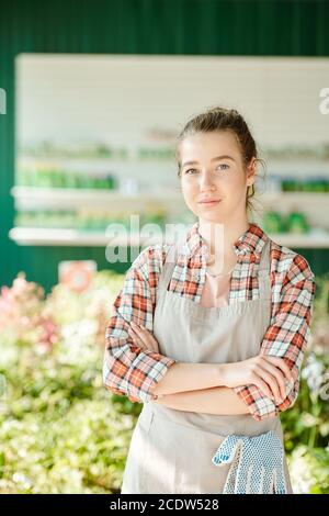 Junge ernsthafte Bäuerin oder Gewächshausarbeiterin in Arbeitskleidung suchen Bei Ihnen Stockfoto