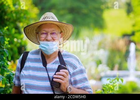 Porträt eines alten Mannes eine tragend medizinische Maske zu schützen Während Coronavirus in einem Park Stockfoto