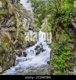 Bergbach mit Wasserfall fließt unter Klippen der Schlucht unter Felsbrocken Stockfoto