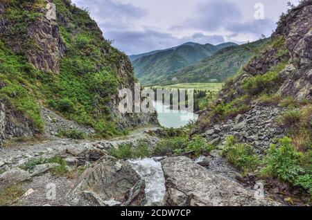 Gebirgsbach, der unter Klippen der Schlucht in den Fluss Katun im Altai-Gebirge, Russland fließt Stockfoto