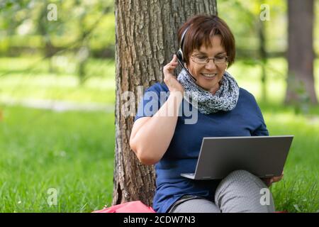 Nahaufnahme eines Porträts einer Frau im Stadtpark, die online mit Headset und Laptop sprach. Stockfoto