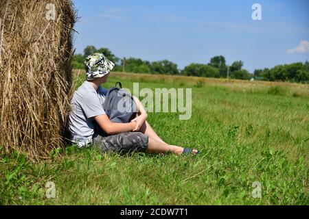 Teen mit Rucksack sitzt neben Stapel von Stroh Stockfoto