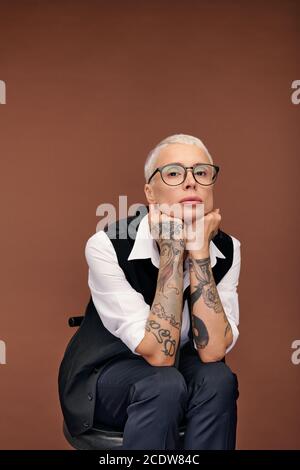 Junge blonde Frau mit kurzen Haaren und Armen bedeckt mit Tattoos sitzen auf einem Stuhl Stockfoto