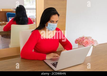 Schöne lateinische Frau mit Gesichtsmaske Durchführung Home Office Stockfoto