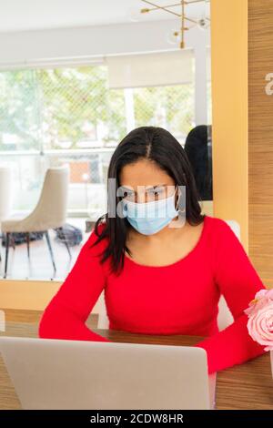 Schöne lateinische Frau mit Gesichtsmaske Durchführung Home Office Stockfoto