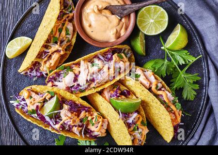 Lachs-Tacos mit Rotkohlsalat mit würziger Joghurtsauce bestreut mit fein gehackter Petersilie auf einem schwarzen Teller auf einem dunklen Holztisch, hori, serviert Stockfoto