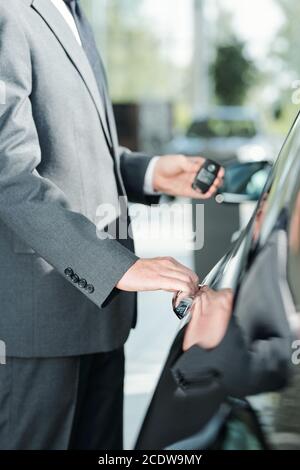 Junge elegante Verkäufer von neuen Autos in Anzug mit Fernbedienung Steuerung zum Öffnen der Tür Stockfoto