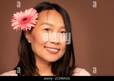 Glückliche junge asiatische Frau mit schönen rosa Herbera in dunkel Langes Haar Stockfoto