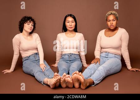 Gruppe von zeitgenössischen jungen Frauen verschiedener Ethnien sitzen auf Der Boden Stockfoto