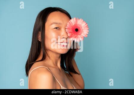 Junge hübsche asiatische Frau mit toothy Lächeln halten wunderschöne rosa Herbera Stockfoto