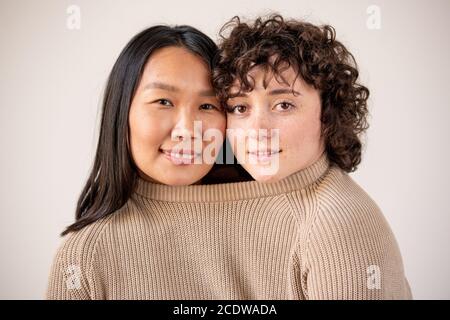 Junge asiatische und kaukasische Frauen mit dunklen Haaren in einem Strickpullover aus Baumwolle Stockfoto