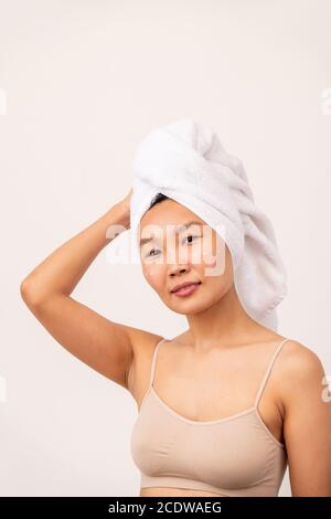 Junge hübsche Frau der asiatischen Ethnie mit Handtuch auf dem Kopf Und beigefarbenes Tanktop Stockfoto
