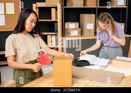 Junge asiatische Frau Versiegelung verpackten Auftrag im Karton gegen Kollege Stockfoto
