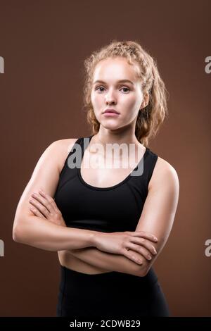 Schlanke junge ernsthafte Sportlerin in schwarzem Trainingsanzug hält ihre Arme Gekreuzt Stockfoto