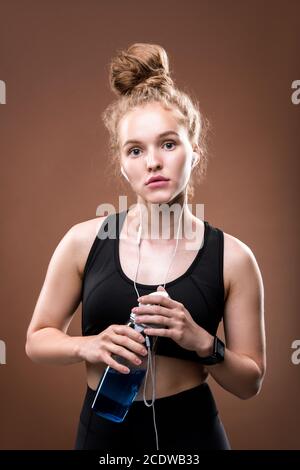 Junge fit Frau in Kopfhörer und schwarzen Trainingsanzug mit Flasche Von Wasser Stockfoto