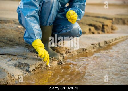 Die Hände der jungen Ökologin, die am Bach sitzt, sind mit Handschuhen übersät Schmutziges Wasser Stockfoto