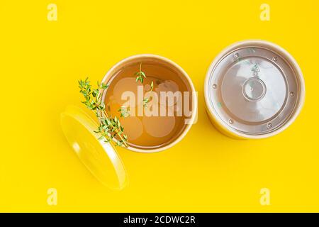 Gemüse- oder Hühnerbrühe oder Brühe mit Thymian in einem Einwegbecher aus Bastelpapier auf gelbem Hintergrund. Suppe zu gehen, gesunde Ernährung Lieferung. Stockfoto