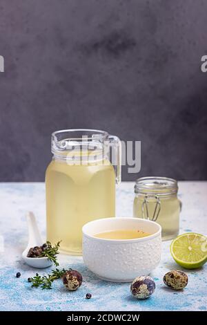 Hausgemachte Hühnchen- oder Gemüsebrühe oder Brühe in Schüssel und Glas Vorratsgläser auf blauem Hintergrund. Stockfoto