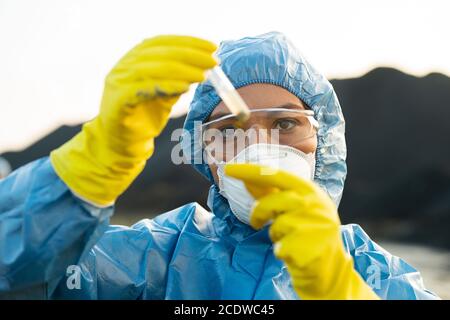 Junge Forscherin in schützende Arbeitskleidung Blick auf Kolben mit Probe Stockfoto