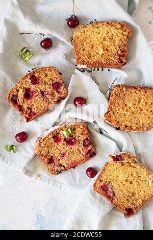 Stücke von Nusskuchen mit Kirsche über Leinen Serviette, hellen Beton Hintergrund. Hausgemachte frische Bäckerei für Wüste. Stockfoto