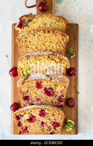 Scheiben hausgemachter Pfundkuchen mit Kirschen und Nüssen auf Holzschneidebrett. Hellblauer Hintergrund. Draufsicht. Stockfoto