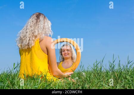 Blonde Frau sitzt und schaut auf den Spiegel draußen Stockfoto