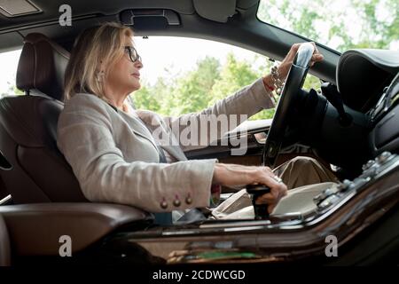 Seitenansicht einer reifen Frau, die an einem offenen Fenster sitzt Auto und Fahren zur Arbeit Stockfoto