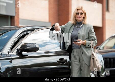 Elegante reife Geschäftsfrau oder Agent in Sonnenbrille, Anzug und Perlenkette Stockfoto