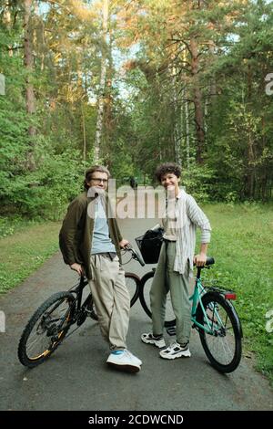 Junge fröhliche Paar mit Fahrrädern stehen zwischen Bäumen vor Der Kamera Stockfoto