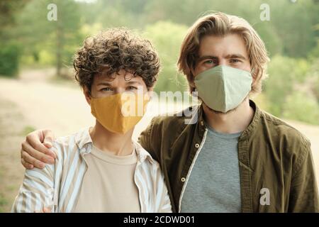 Junge liebevolle Paar in Schutzmasken und Casualwear Blick auf Sie Stockfoto