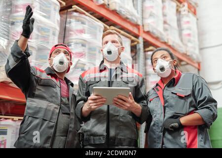 Junge, zeitgenössische interkulturelle Lagerarbeiter diskutieren bei der Arbeit Stockfoto