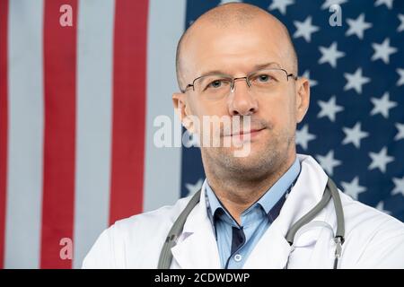 Moderner Arzt mittleren Alters in Brillen, der dich anschaut US-Flagge Stockfoto