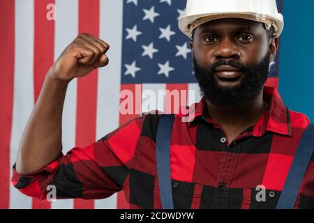 Junge Baumeister afrikanischer Ethnie in Arbeitskleidung und Hardhat zeigen Seine Stärke Stockfoto